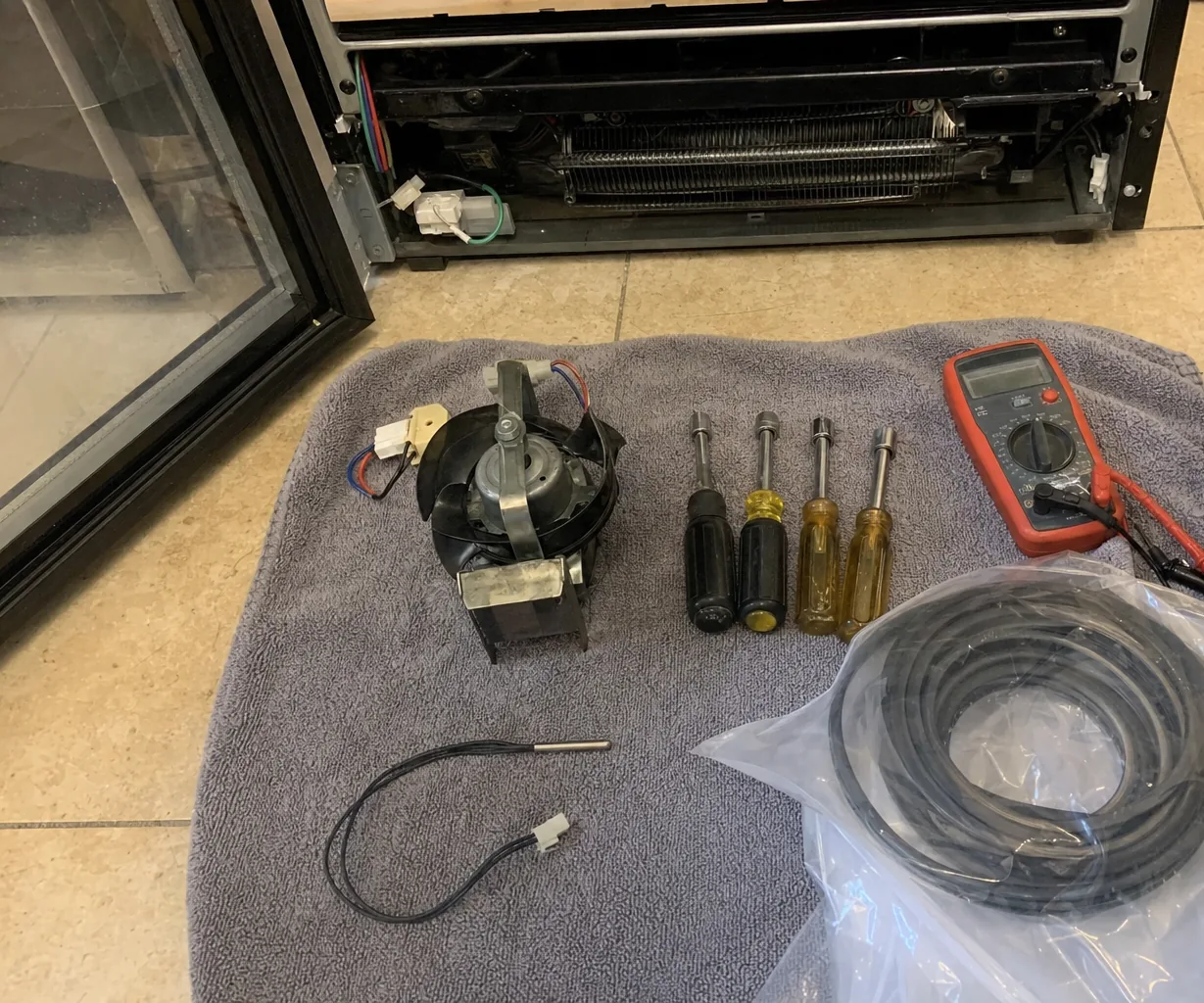 A replacement evaporator fan motor and a temperature sensor on a towel, beside an appliance with its rear panel removed
