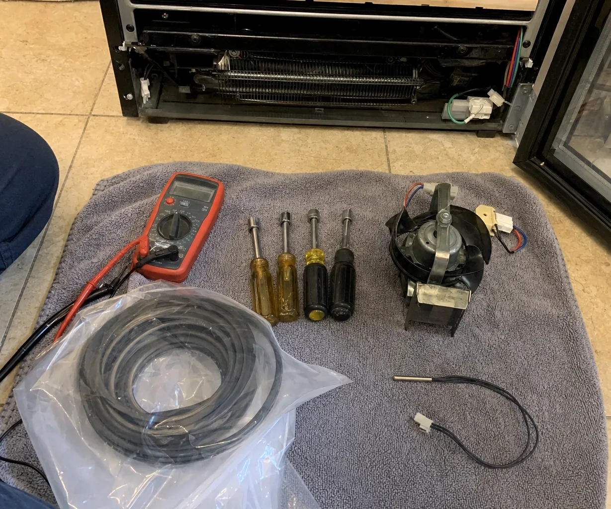Replacement parts still bagged beside the meter — an OEM fan motor, a door gasket and a temperature sensor