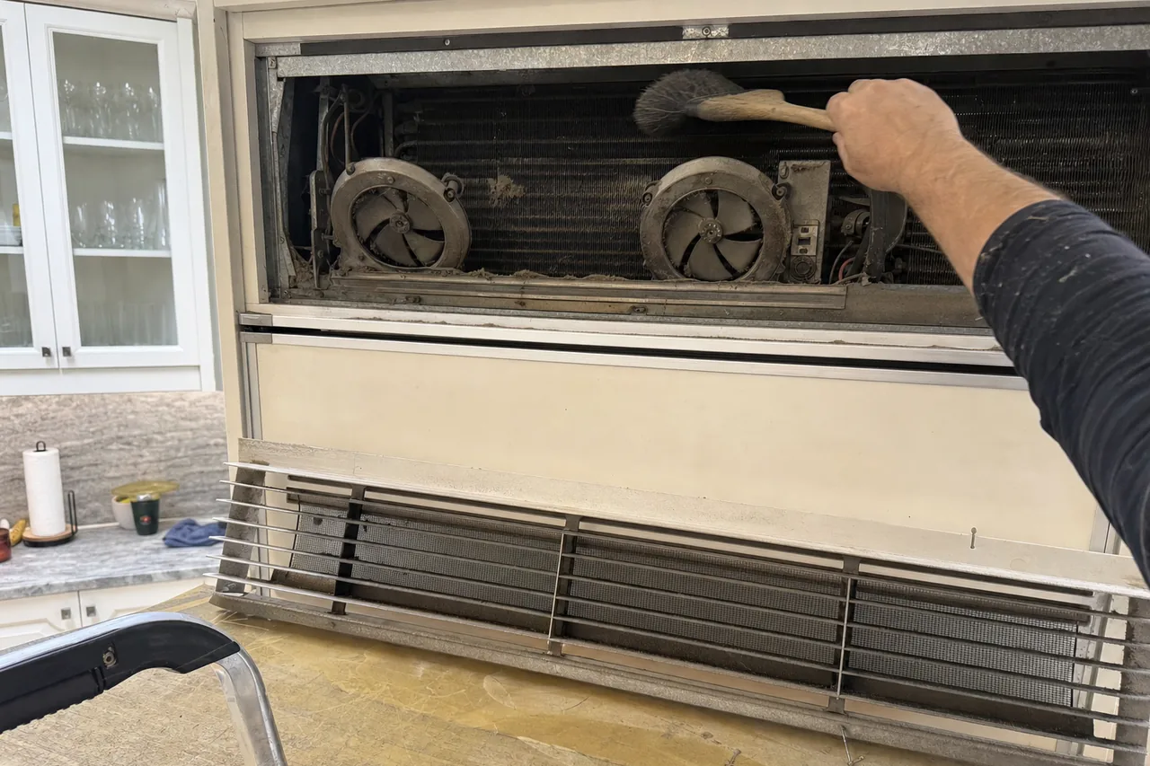Dust being brushed off the condenser coil and twin fans behind the top grille of a built-in refrigerator