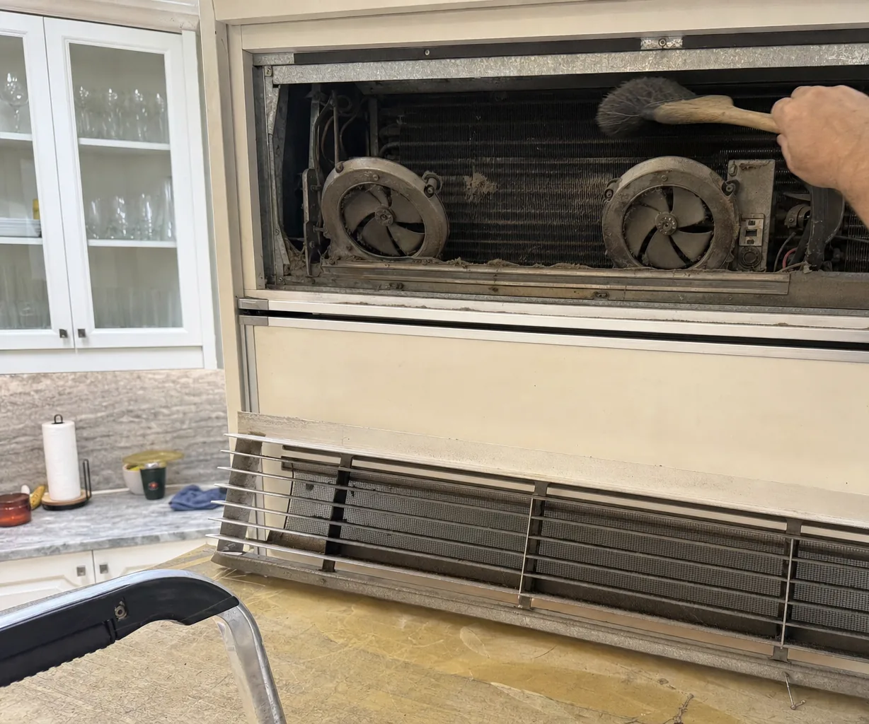 Glass-front cabinets beside a built-in refrigerator whose upper grille has been removed for a condenser service