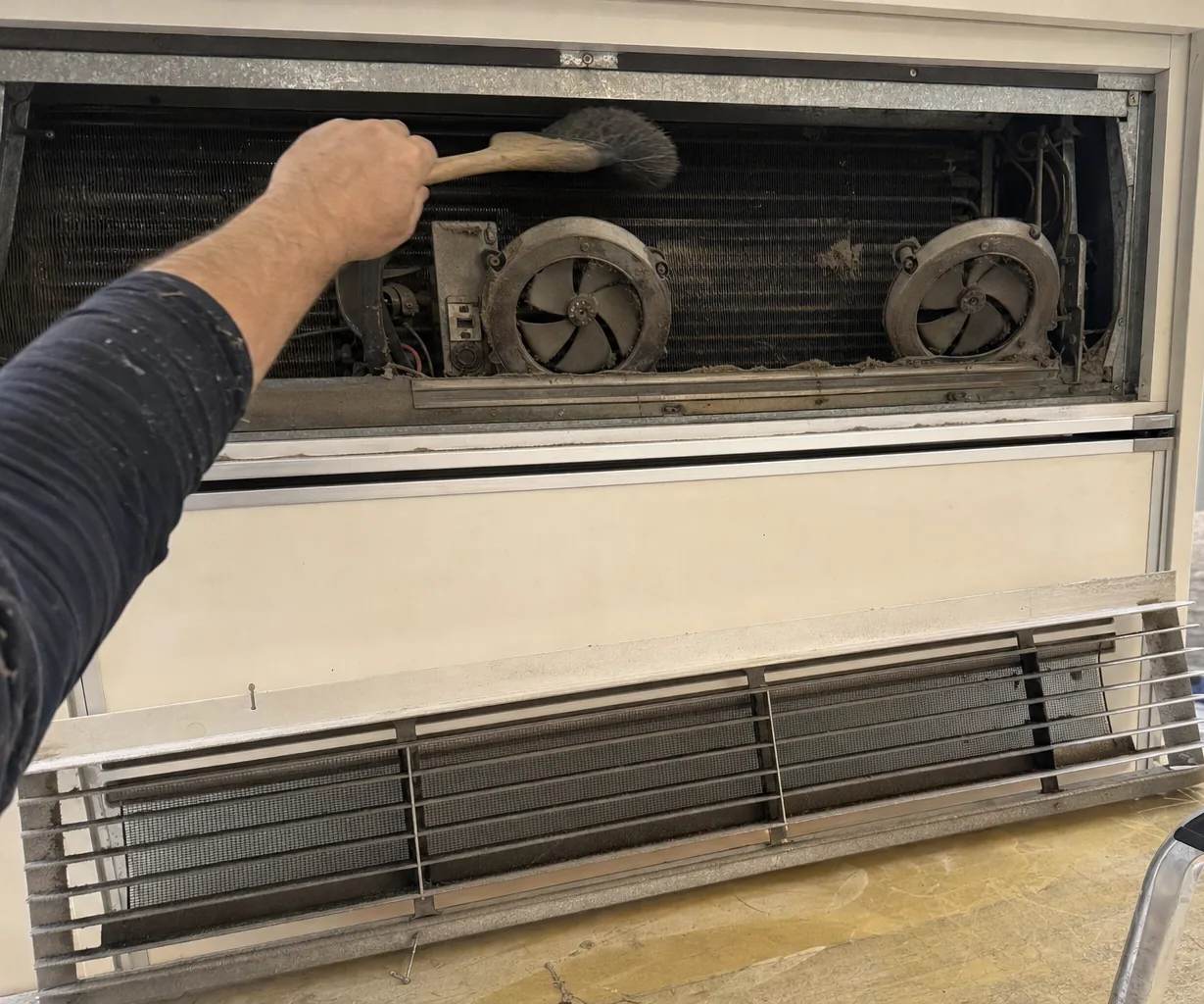 The exposed machine compartment of an older built-in refrigerator — condenser coil, two fans and the control pocket