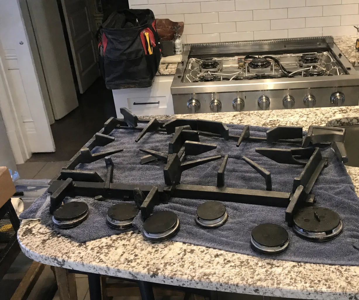 A kitchen doorway, a tool bag on the counter and a full set of cast grates laid out on the island